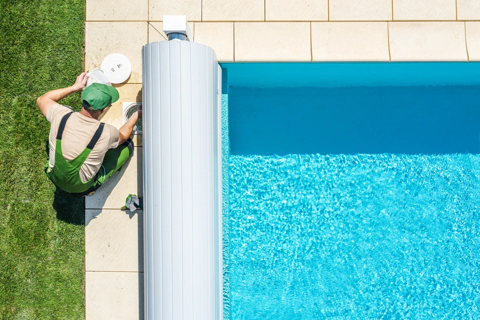 Un travailleur peint sur un pont de piscine en bois extérieur, vue de dessus