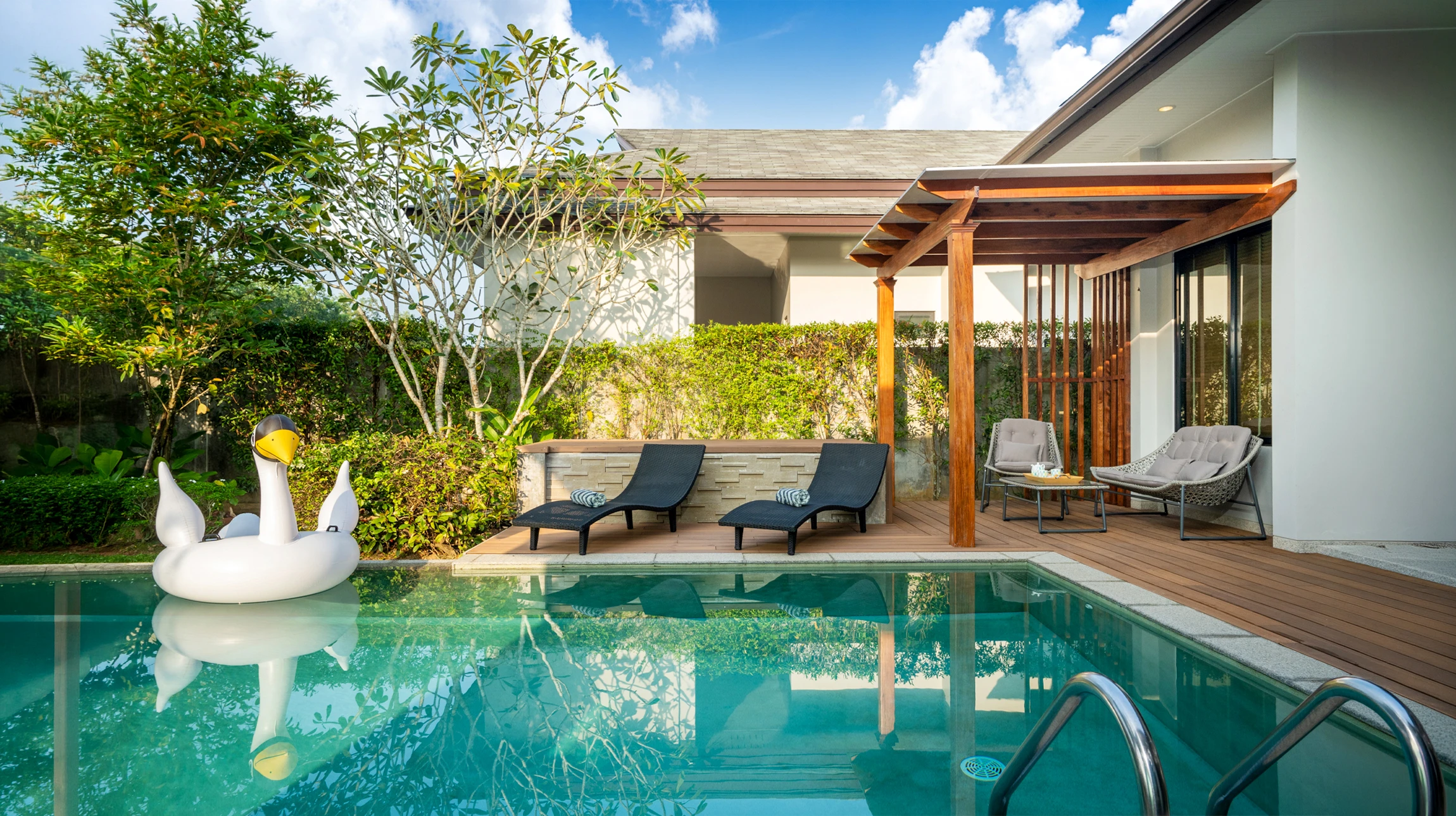 Piscine rectangulaire avec margelles en béton et plage en bois composite, située dans jardin privé avec pelouse entretenue