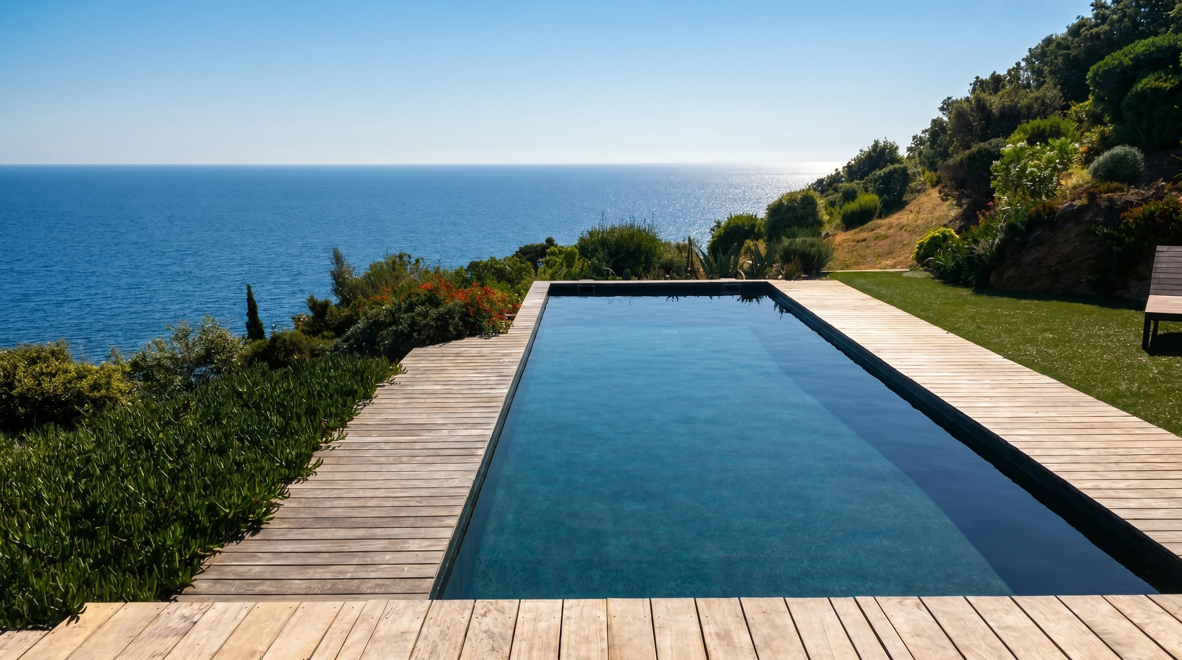 Espace extérieur résidentiel avec piscine rectangulaire à débordement, entourée de dallage en pierre naturelle claire