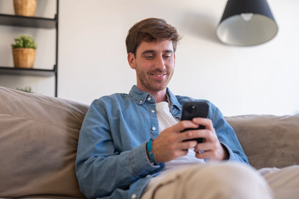 Gros plan d'une main tenant un smartphone en orientation paysage, affichant clairement un tableau de bord ou une interface de suivi de projet avec des éléments visuels tels que barres de progression, statuts de chantier, ou chronologies de travaux. L'écran doit être lisible et professionnel, montrant des données structurées typiques d'une application métier. Arrière-plan légèrement flou, lumière naturelle, style réaliste et professionnel.
