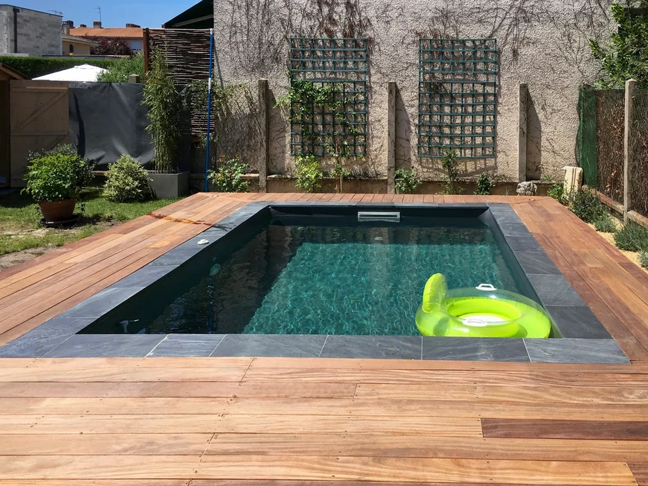 Scène extérieure au bord d'une piscine résidentielle avec margelles en pierre naturelle et végétation en arrière-plan